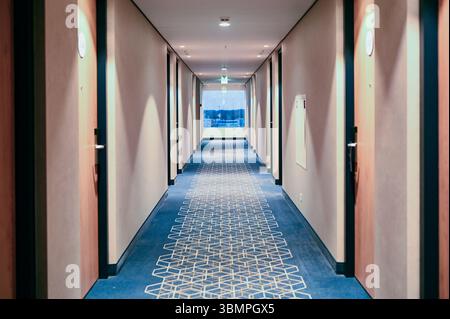 Long hallway with blue carpet and window in hotel Stock Photo