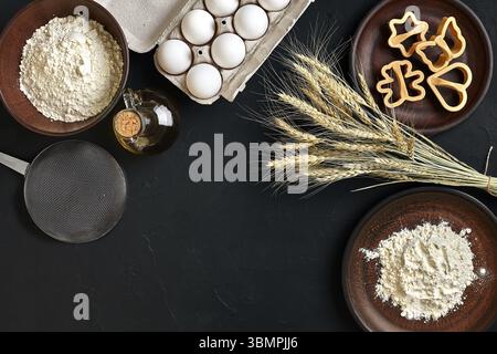 Flour, eggs, rolling pin, plastic baking forms on black table. Top view with space for your text. Still life. Flat lay Stock Photo