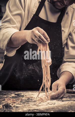 The chef makes fresh spaghetti from scratch. Wooden table. Photo in brown tones. Kitchen Stock Photo