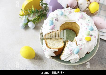 Happy Easter holidays, tasty dessert. Glazed easter lemon cake decorated with confectionery and mini chocolate eggs candy on gray stone background. Co Stock Photo