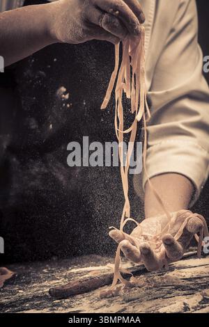 The chef makes fresh spaghetti from scratch. Wooden table. Photo in brown tones. Kitchen Stock Photo