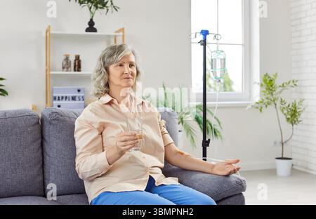Elderly woman sitting on taking medicine through a drip, close-up Stock Photo