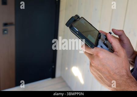 Close-up of hands holding drone controller. Mans hands operating a drone controller with attached screen, standing in front of a modern wooden Stock Photo