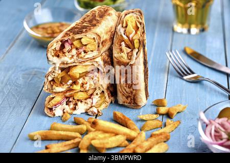 Middle Eastern Chicken Shawarma, Pita Sandwich, chicken roll in a pita with fresh vegetables, cream sauce and french fries on wooden background. Selec Stock Photo