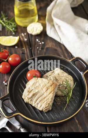 Cooked juicy tuna steak with spices, tomatoes and rosemary on a stone plate. Restaurant food. Seafood. Rustic style Stock Photo
