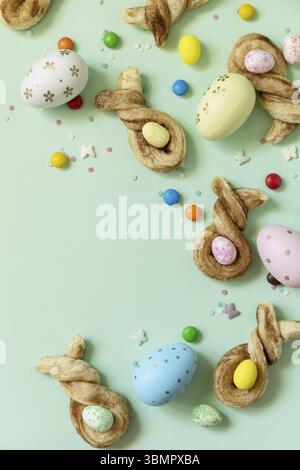 Happy Easter Holidays. Colors Easter eggs with Easter rabbit-shaped buns puff pastry with cinnamon on pastel green background. View from above. Copy s Stock Photo
