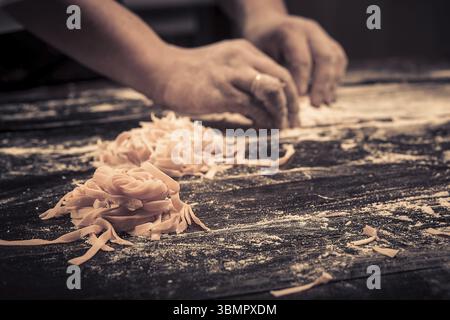 The chef makes fresh spaghetti from scratch. Wooden table. Photo in brown tones. Kitchen Stock Photo