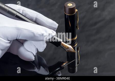 Black fountain pen on marble gray background. Hand in white glove. Stationery Stock Photo