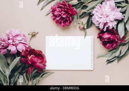 Notebook and frame of beautiful peonies on beige background. Spring or summer floral background Stock Photo