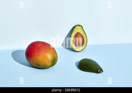 Half of fresh avocado and mango fruits on blue background Stock Photo