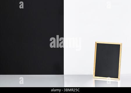 Blank blackboard on table near white and black wall. Template mock up for adding your design and leave space beside frame for adding more text Stock Photo