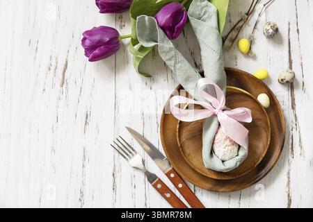 Easter table setting with painted eggs, purple tulip and cutlery on festive table. Table setting for Happy Easter day. Top view flat lay. Copy space Stock Photo