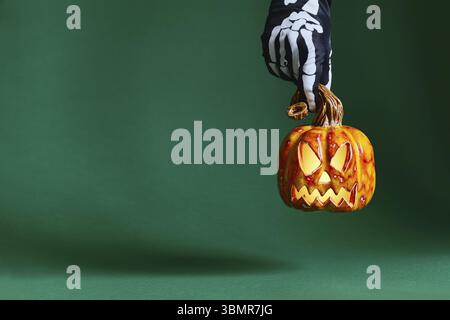 Skelett Handschuh haelt Keramik Kuerbis Jack-o'-Lantern auf gruenem Hintergrund Stock Photo