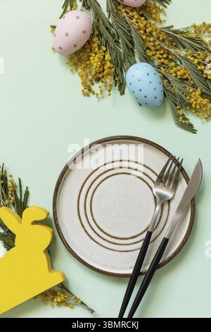 Easter table setting. Plate with easter eggs and mimosa on a pastel green background. Happy Easter holiday concept for restaurants. View from above. C Stock Photo