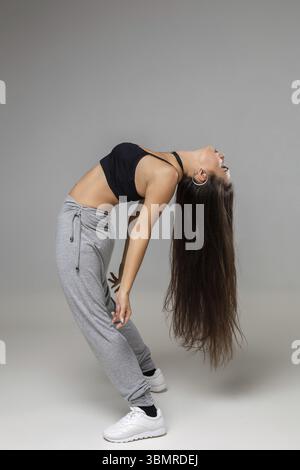 Modern dancer poses in front of the gray studio background. Modern dance styles, dancehall, jazz funk, hip hop Stock Photo