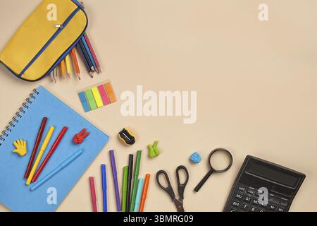 Bright flat lay photo of a workspace desk with school stationers, such as blue notebook, colored pencils, yellow pencil case, felt-tip pens, magnifier Stock Photo
