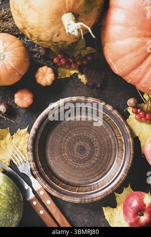 Thanksgiving day concept. Autumn table setting for dinner with plate, knife, fork decorated pumpkins and maple leaves. Flat lay autumn composition Stock Photo