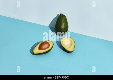 Composition of fresh fruits, whole avocado and two halfs of cutted avocado on blue background. Mock up, two-colored pastel Stock Photo