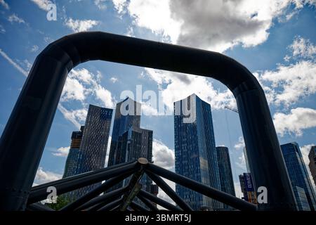 The skyscrapers around Deansgate Square rise into a sunny sky and are framed by the steel tubes of the footbridge to Deansgate Castlefield Station. Stock Photo
