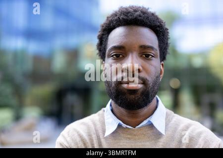 A serious man looks directly at the camera. He has a beard and is in an urban setting. Stock Photo