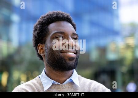 A smiling man looks off into the distance, possibly in a city environment, exuding positivity and confidence. Stock Photo