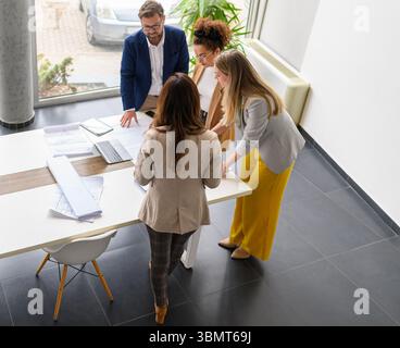 High angle view of group of architects analyzing blueprint and discussing ideas while standing at table in office Stock Photo