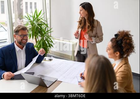 Businesswoman discussing blueprints and business plans with cheerful team of architects in meeting at office Stock Photo