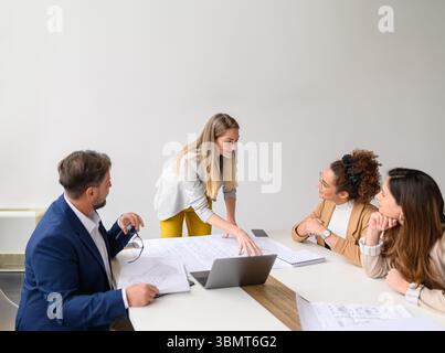 Female engineer reviewing blueprint with colleagues in meeting discussing construction plans and collaborating in office Stock Photo