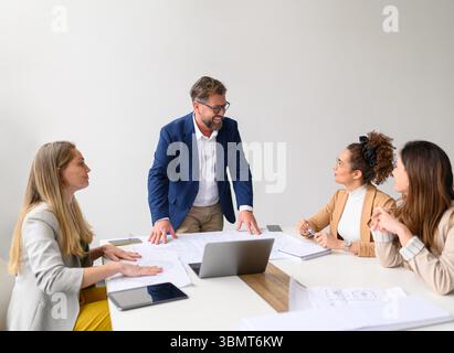 Male architect smiling and discussing project ideas with female professionals while collaborating in meeting Stock Photo