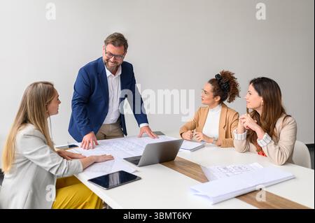 Female professionals discussing blueprints with male engineer while collaborating in meeting at conference room Stock Photo