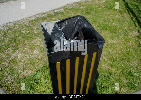 High-angle close-up of a black trash can with a dark-colored plastic liner. The can is rectangular and made of dark-gray metal. Stock Photo