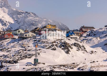 Bright wooden houses on a snowy slope in Sisimiut, Greenland, with rugged Arctic mountains behind. Remote winter settlement. Stock Photo
