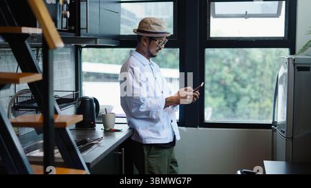 Stylish man using mobile phone in contemporary kitchen, enjoying modern living and connectivity Stock Photo