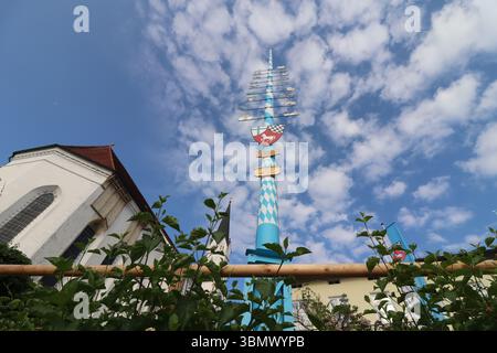 KIRCHDORF, GERMANY - JUNE 19, 2025: Traditional Bavarian maypole and church building in Kirchdorf captured from below against a partly cloudy blue sky Stock Photo