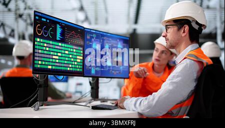 Multiracial Team Using PCs To Monitor Data In Manufacturing Facility Stock Photo