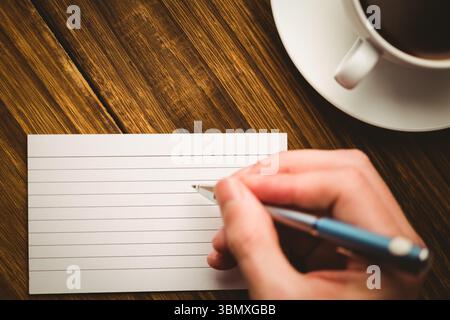 Human hand writing on paper at desk with coffee cup Stock Photo