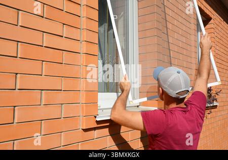 Mosquito wire screen installation. Worker installing mosquito wire screen on house window to protect from insects. Stock Photo