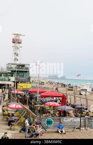 Seaside Cafe with Crowded Beach and Restaurant Patrons Under Umbrellas. Brighton, England Stock Photo