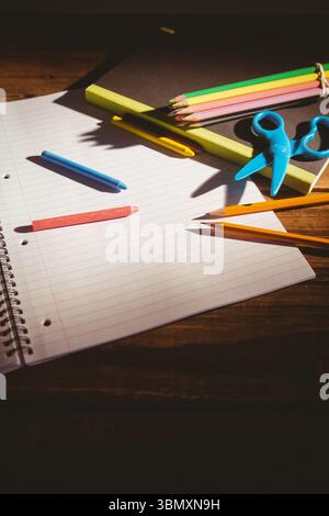 Spiral-bound notebook is lying open on dark wooden desk with crayons, pastel pencils and scissors Stock Photo