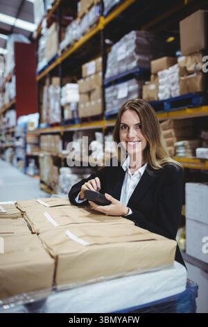 Woman in business attire standing at large warehouse scanning brown packages with handheld scanner Stock Photo
