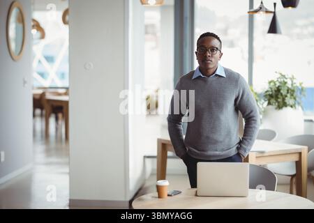 African American man wearing business attire working on laptop in cafe with coffee cup, smartphone Stock Photo