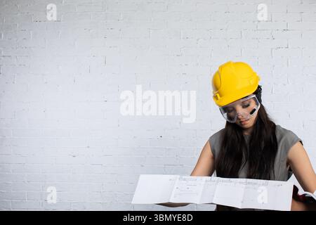A Female Engineer Diligently Reviewing Detailed Construction Plans While Wearing a Hard Hat Stock Photo