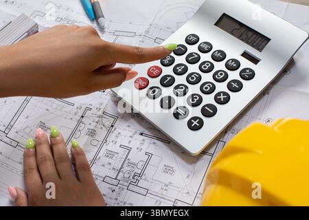 Using a Calculator on a Construction Blueprint While Wearing a Safety Helmet for Effective Planning Stock Photo