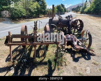 Old rusty antique Farm tractor and plough and bit of farming equipment abandoned by the side of a back road on a hot summer day Stock Photo