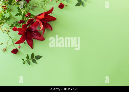 Bright petals of two red lilies with red roses on green background. Stock Photo
