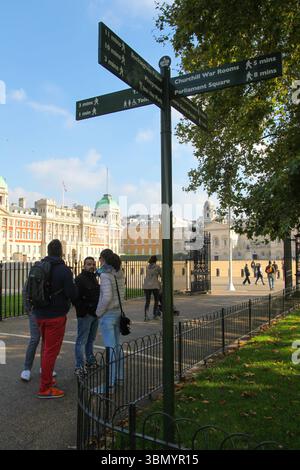 Signpost and tourists at Horse Guards Parade entrance gate in London, with sunlit courtyard and historic atmosphere. Stock Photo