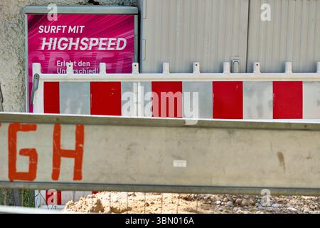 Mindelheim, Bavaria, Germany - 28 June 2025: Symbolic image of fiber optic expansion: Behind a construction site barrier, a distribution box advertises with the Deutsche Telekom slogan:Surft mit Highspeed. Digital infrastructure and telecommunications *** Symbolbild Glasfaser-Ausbau: Hinter einer Baustellenabsperrung wirbt ein Verteilerkasten mit dem Slogan der Deutschen Telekom:Surft mit Highspeed. Digitale Infrastruktur und Telekommunikation Stock Photo