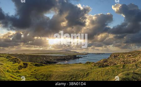 Dramatic sunset over Ireland's Wild Atlantic Way, with golden light breaking through storm clouds above the rugged Atlantic coastline and sea. Stock Photo