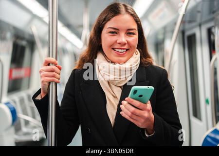 Happy female commuter using her smartphone on the subway, immersed in her mobile device while traveling, showcasing the convenience of technology in Stock Photo