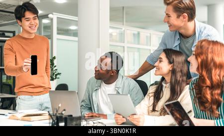 Diverse group of students sitting at desk guy showing phone Stock Photo